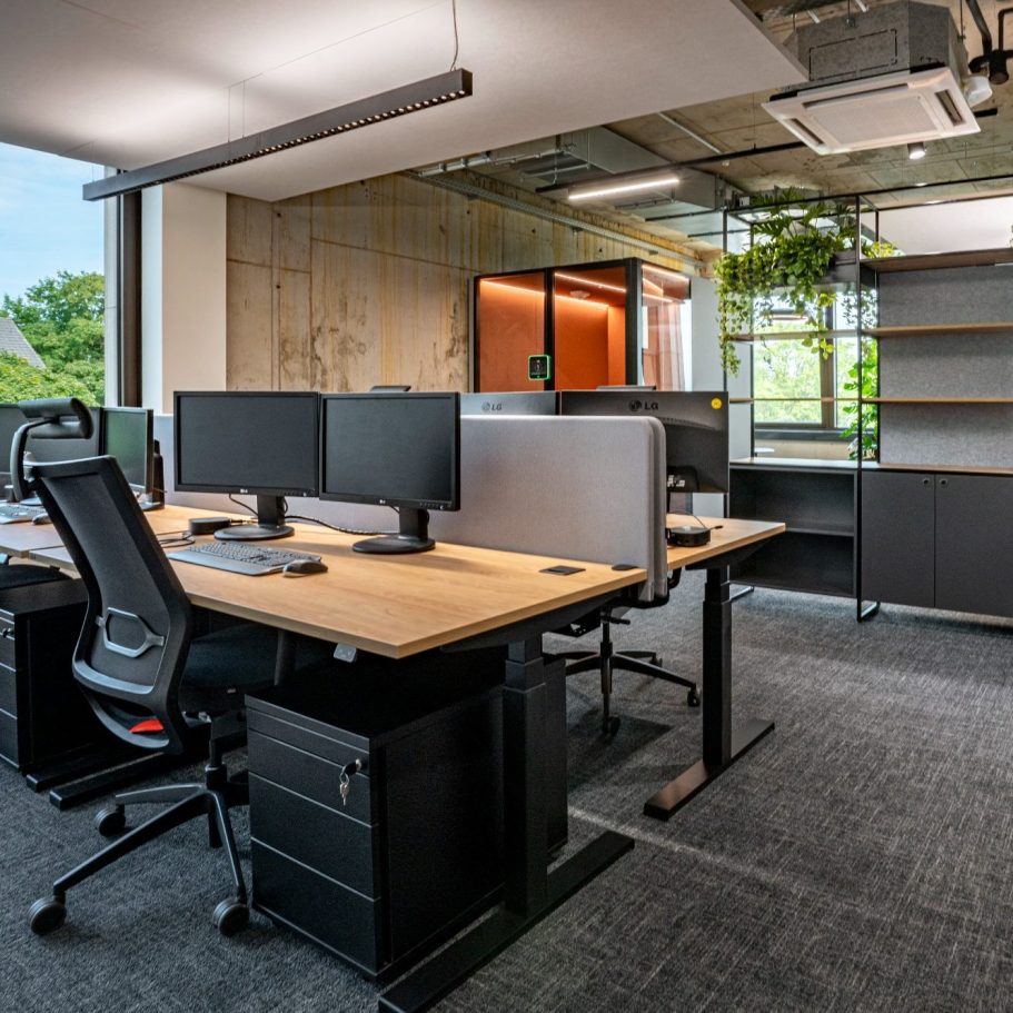 Zirkuläre Arbeitswelten Modernes Büro mit modular angeordneten Schreibtischplätzen, Doppelbildschirmen, einer Telefonbox und Stauraumlösung.